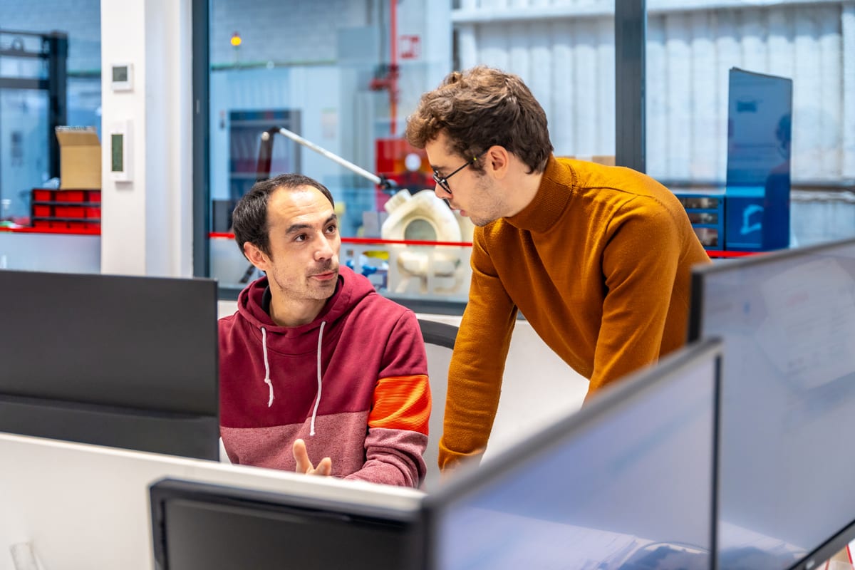 Two technicians talking over a workstation in a machine shop office