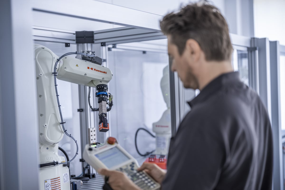 An engineer programming a Kawasaki robot cell with a handheld teach pendant
